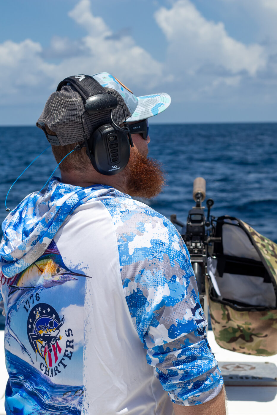 1776 Charters crew member in ear protection beside the mounted machine gun on deep blue water