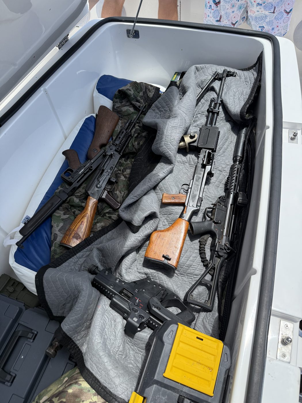 Rifle and belt-fed machine gun laid out on the deck cushion of the boat
